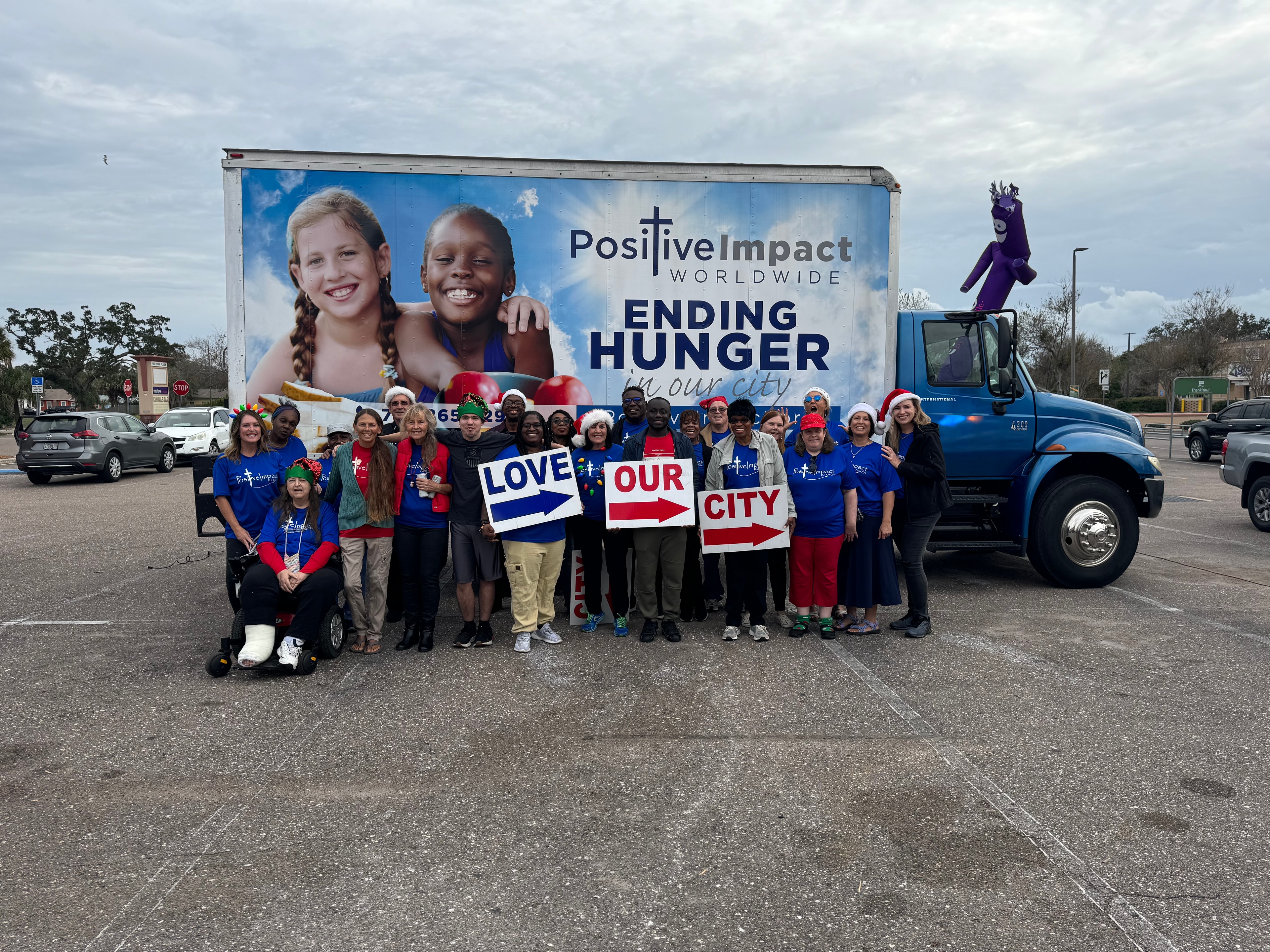 Positive Impact volunteers holding Love Our City signs in front of the Positive Impact Worldwide truck