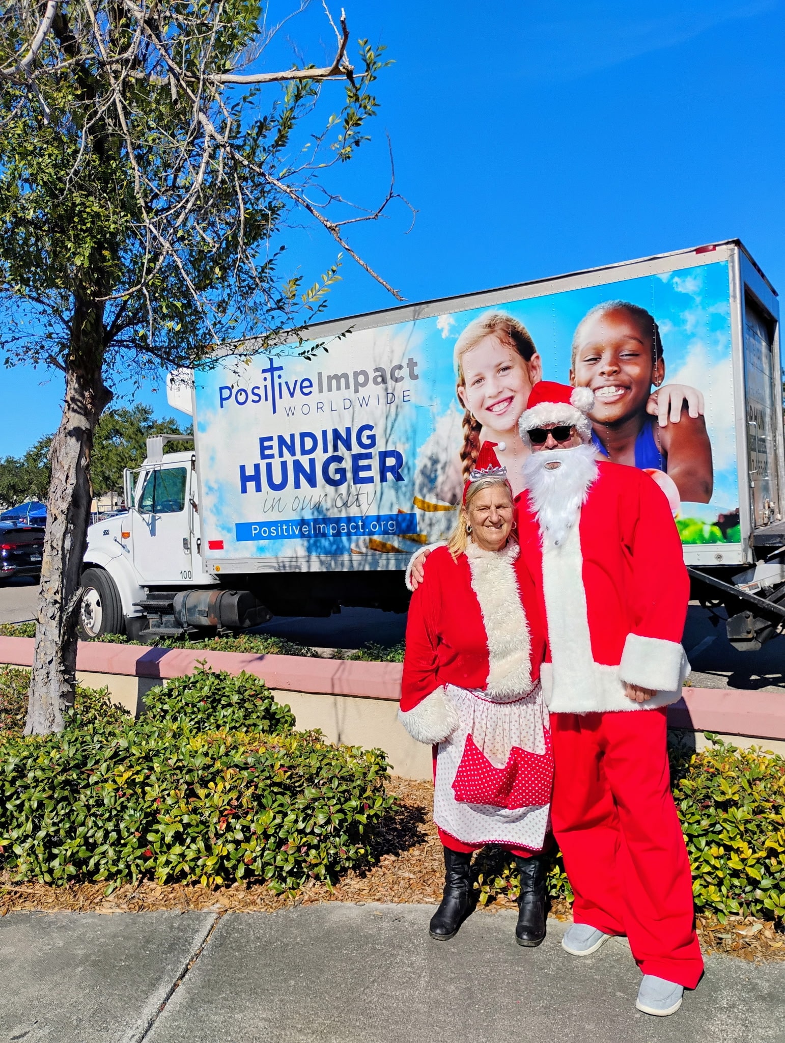 Santa and volunteers in front of the Positive Impact Worldwide truck at a holiday distribution event