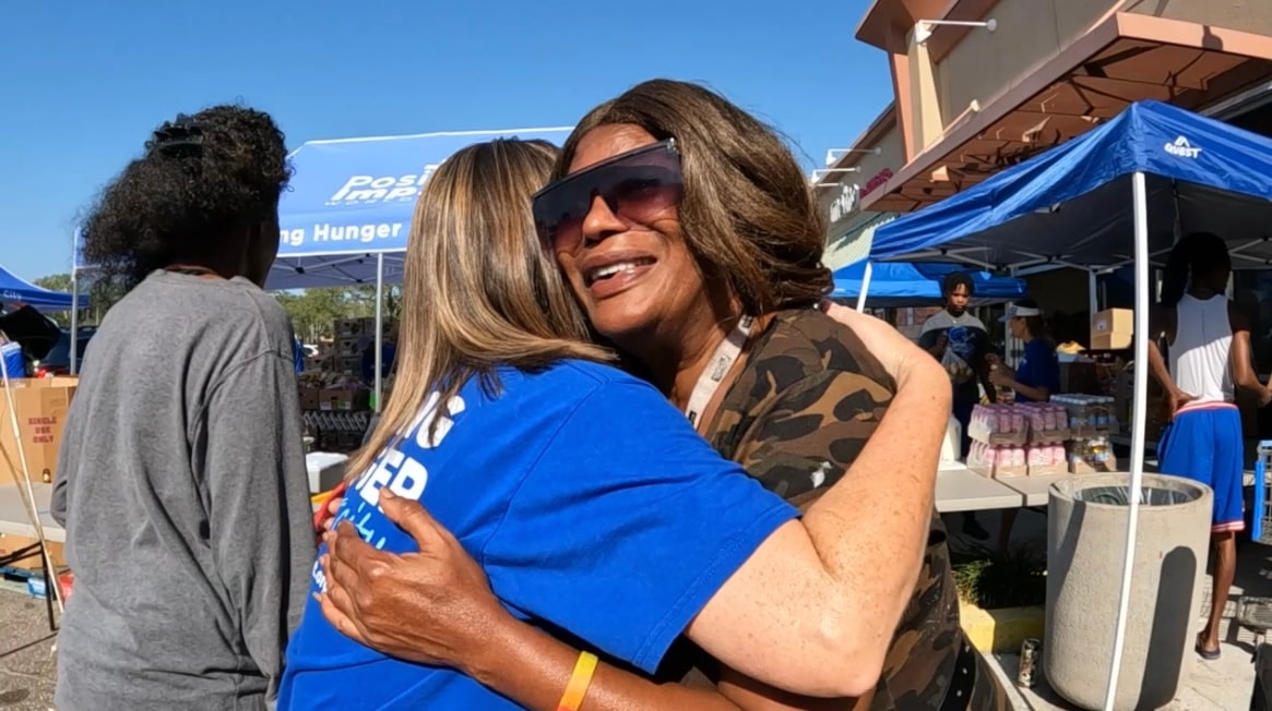 A volunteer in a Positive Impact shirt sharing a warm hug with a community neighbor at the distribution event