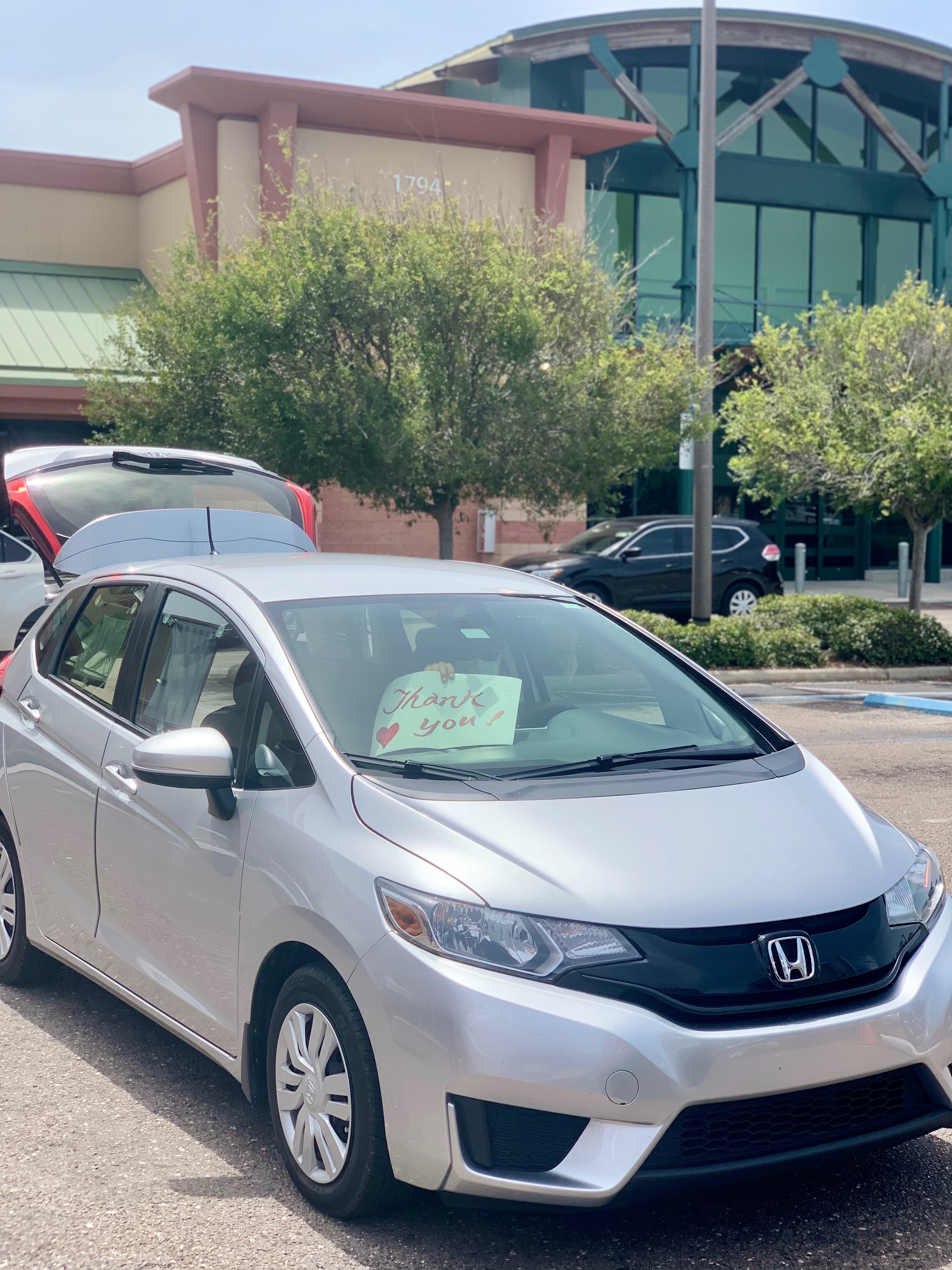 A neighbor holds a handwritten "Thank you!" sign in their car window after receiving food at the Positive Impact drive-through distribution