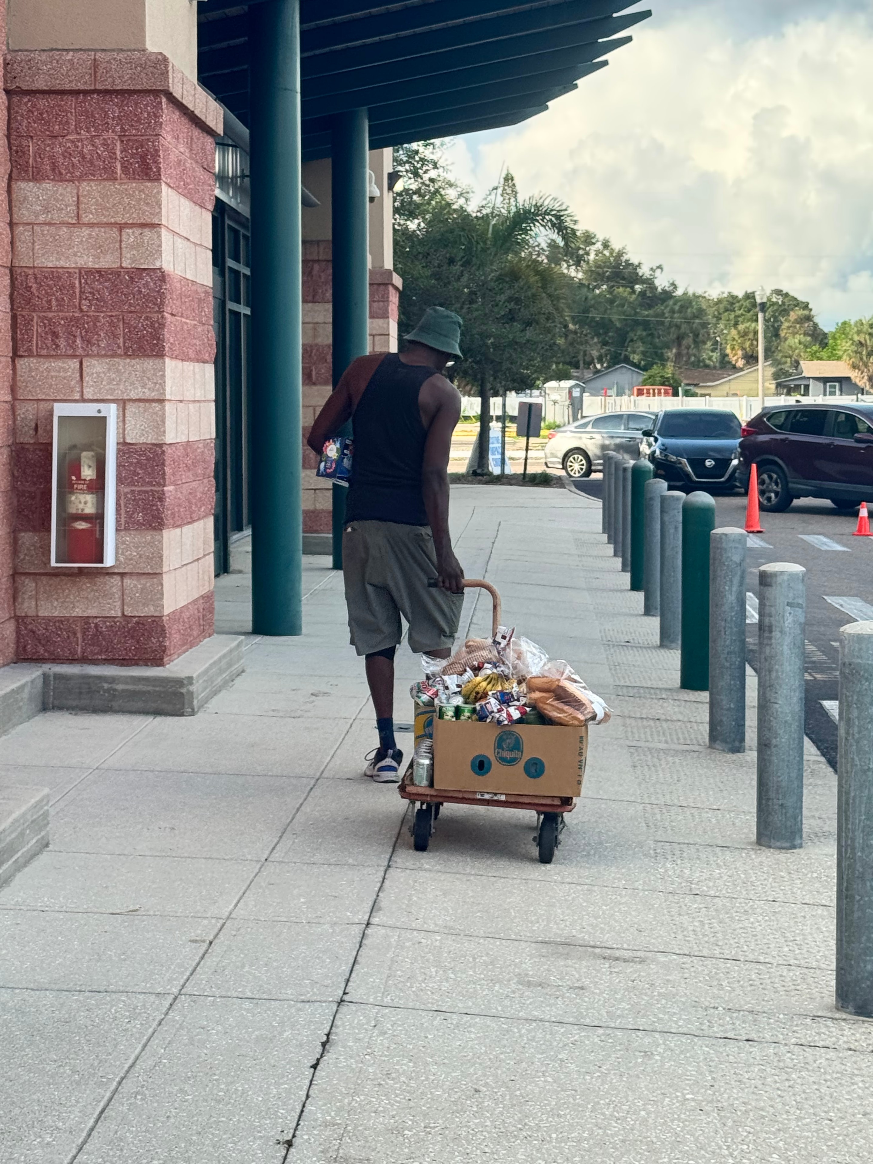 A community neighbor wheels a cart full of groceries away from the Positive Impact food distribution at Tangerine Plaza