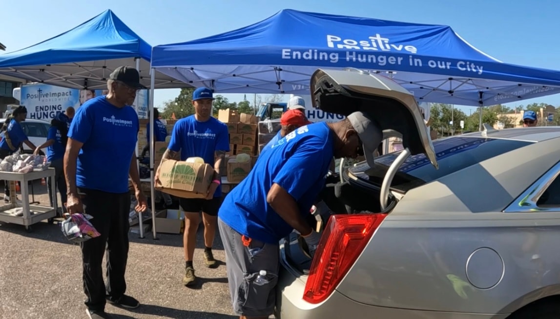 Volunteers in blue shirts loading food into a car trunk
